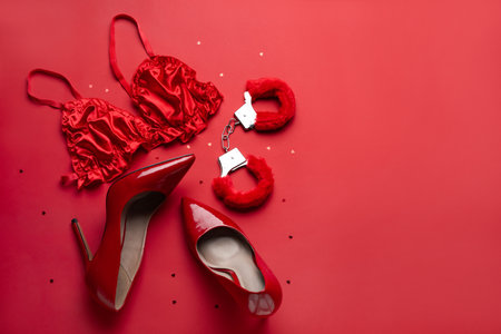 Handcuffs from sex shop, heels and bra on red backgroundの写真素材