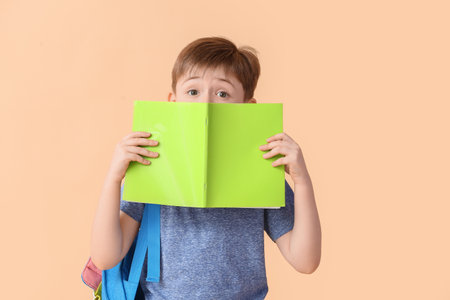 Little schoolboy with notebook on color background