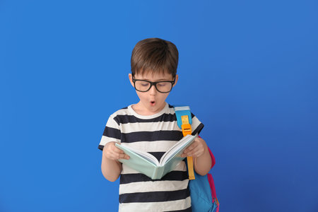 Surprised little schoolboy with book on color backgroundの写真素材