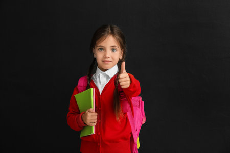 Little schoolgirl showing thumb-up on dark background