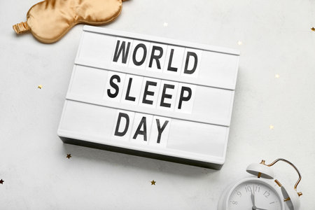 Board with text WORLD SLEEP DAY, alarm clock and sleeping mask on light background, closeupの写真素材