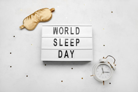 Board with text WORLD SLEEP DAY, alarm clock and sleeping mask on light backgroundの写真素材