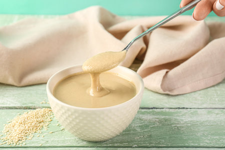 Female hand with bowl and spoon of tasty tahini on color wooden tableの写真素材