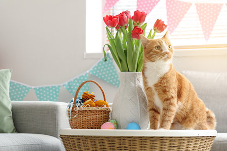Cute cat, vase with tulips and Easter eggs on table at homeの写真素材