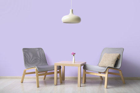 Stylish gray armchairs and table near lilac wallの写真素材