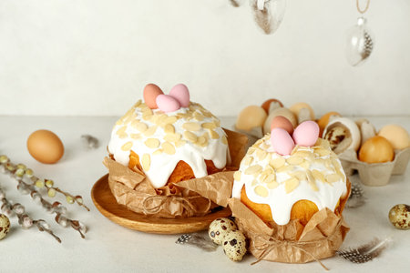 Easter cakes with painted eggs, feathers and pussy willow branches on table near white wall