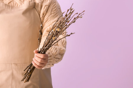 Woman in beige apron holding willow branches on lilac backgroundの写真素材