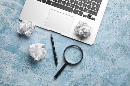 Crumpled paper balls, magnifier, pen and laptop on color background. World Poetry Day celebrationの写真素材
