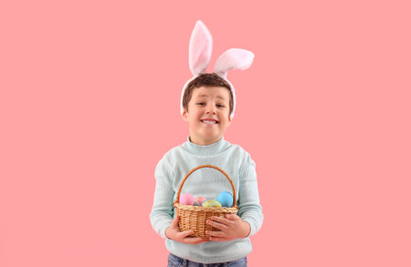 Cute little boy with bunny ears and Easter basket on pink background