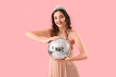 Beautiful young woman in prom dress and with disco ball on pink backgroundの写真素材