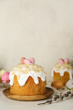 Easter cakes, painted eggs and pussy willow branches on table near white wall