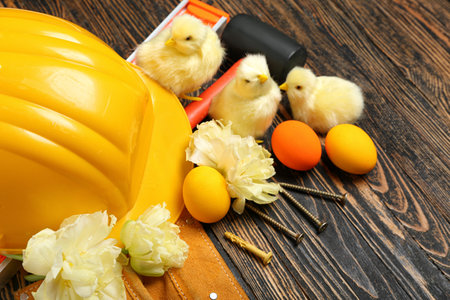 Builder's equipment with Easter eggs, chickens and flowers on dark wooden background, closeup