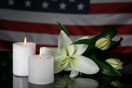 Burning candles with lilies on table against USA flag. National Day of Prayer and Remembrance for the Victims of the Terrorist Attacksの写真素材