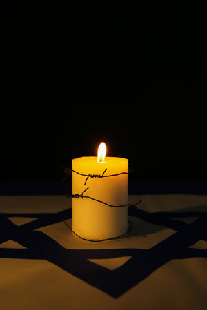 Burning candle with barbed wire on flag of Israel against dark background.