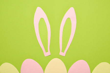 Paper bunny ears and Easter eggs on green background