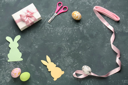 Frame made of Easter eggs, paper rabbits, gift, scissors and ribbon on dark backgroundの写真素材