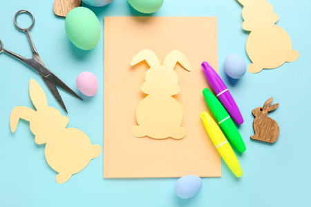 Blank card with paper rabbits, Easter eggs, scissors and markers on blue backgroundの写真素材