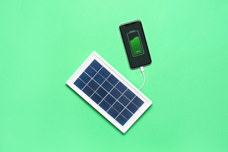 Portable solar panel charging mobile phone on green backgroundの写真素材