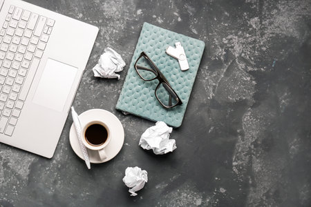 Composition with laptop, notebook, cup of coffee and crumpled paper balls on dark backgroundの写真素材