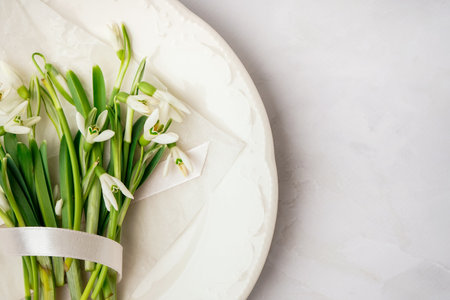 Plate with beautiful snowdrops and ribbon on white background