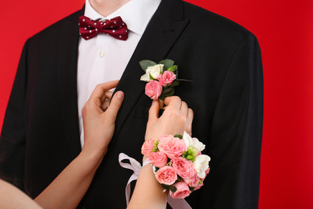 Young woman pinning corsage onto her prom date's suit on red background, closeupの写真素材