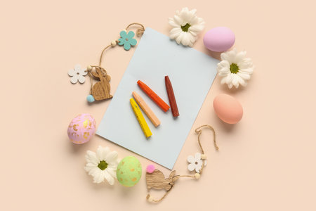 Paper sheet with chalks, Easter eggs and flowers on beige backgroundの写真素材