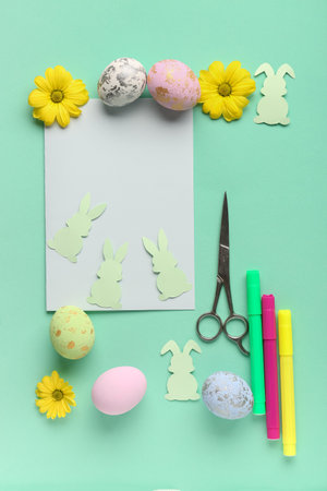 Blank paper sheet with rabbits, Easter eggs, felt-tip pens, scissors and flowers on green backgroundの写真素材