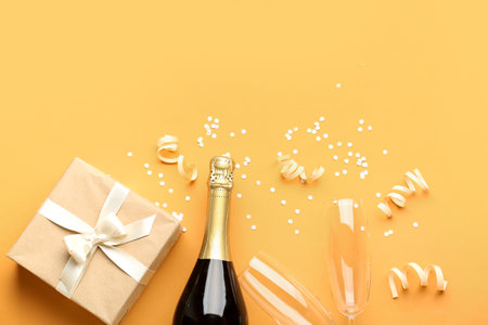 Bottle of champagne, gift box, glasses and serpentine on orange backgroundの写真素材