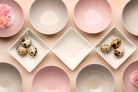 Set of different bowls with carnation flowers and Easter eggs on beige backgroundの写真素材