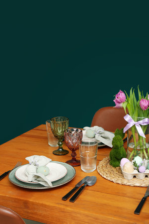 Festive dining table with painted eggs and tulip flowers served for Easter celebration near green...