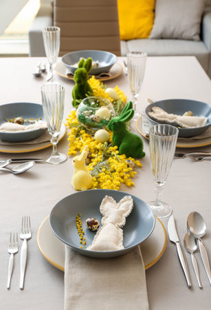 Festive table setting with eggs, bunnies and mimosa flowers served for Easter celebration