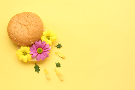 Creative composition with burger bun and beautiful flowers on color background