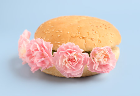 Burger bun with beautiful carnation flowers on light backgroundの写真素材