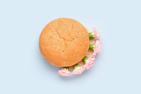 Burger bun with beautiful carnation flowers on light backgroundの写真素材