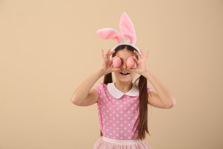 Little girl in bunny ears with Easter eggs on beige backgroundの写真素材