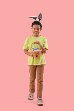 African-American little boy in bunny ears with basket of Easter eggs on pink background