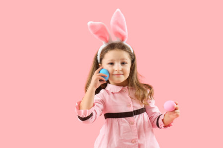 Cute little girl in bunny ears with painted Easter eggs on pink backgroundの写真素材