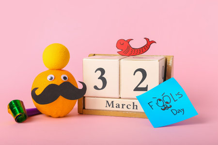 Composition with cube calendar, funny orange and decor on pink background. April Fool's Day celebrationの写真素材