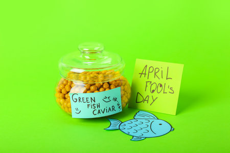 Glass jar of green peas and sticky note with text FOOL'S DAY on color background