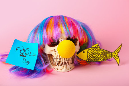 Human scull with clown nose, wig and paper fish on pink background. April Fool's Day celebrationの写真素材