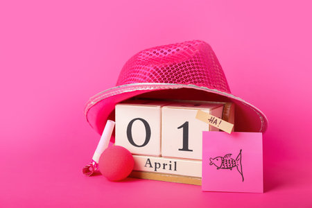 Cube calendar with date 1 APRIL, party decor and hat on pink background. Fool's Day celebrationの写真素材