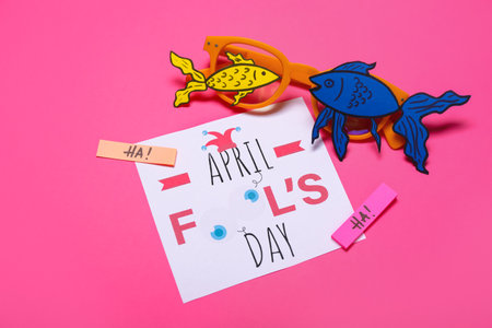 Card with text APRIL FOOL'S DAY, eyeglasses and paper fishes on pink backgroundの写真素材