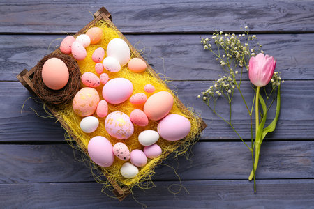 Basket with beautiful Easter eggs, tulip and gypsophila flowers on wooden background