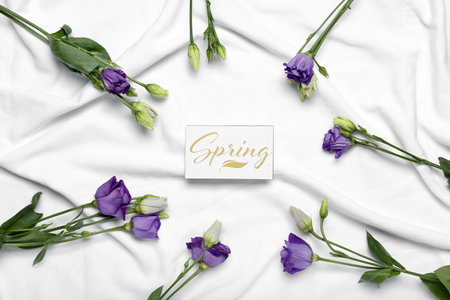 Card with word SPRING and beautiful eustoma flowers on light fabric backgroundの写真素材