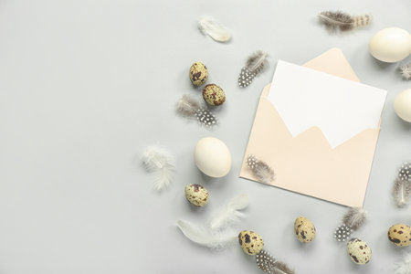 Easter eggs, envelope with blank greeting card and feathers on gray backgroundの写真素材