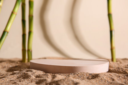 Green bamboo stems and plaster podiums in sand on beige background