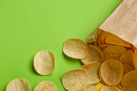 Overturned paper bag with delicious potato chips on green and yellow backgroundの写真素材