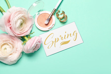 Card with word SPRING, beautiful ranunculus flowers, blush, makeup brush and earrings on color background, closeupの写真素材
