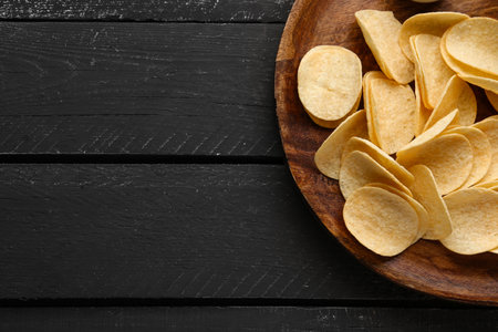 Board with delicious potato chips on black wooden backgroundの写真素材