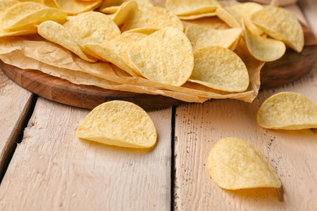 Board with delicious potato chips on white wooden backgroundの写真素材